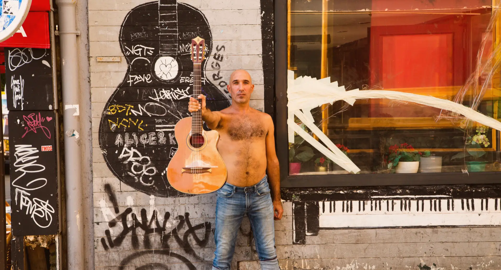 Un homme debout devant un mur taggué qui tient une guitare 