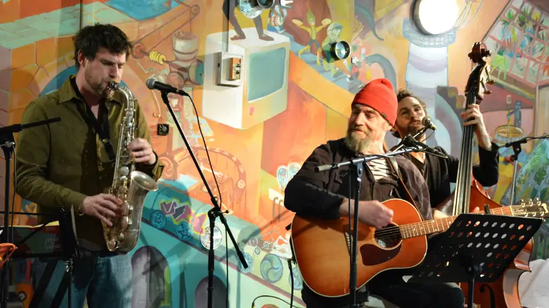 PierPrévo&Cie sur scène avec sa guitare et un chanteur à sa gauche ils sont tous les deux devant un mur très colorés